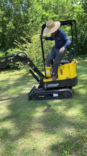 A crew member working from the compact tracked excavator on a lawn
